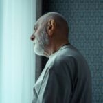 An elderly man gazes out of a window