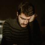 a dark room, man in black sweater with his head in his hands