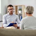 psychologist sits in chair taking notes and patient sits in front with back to camera