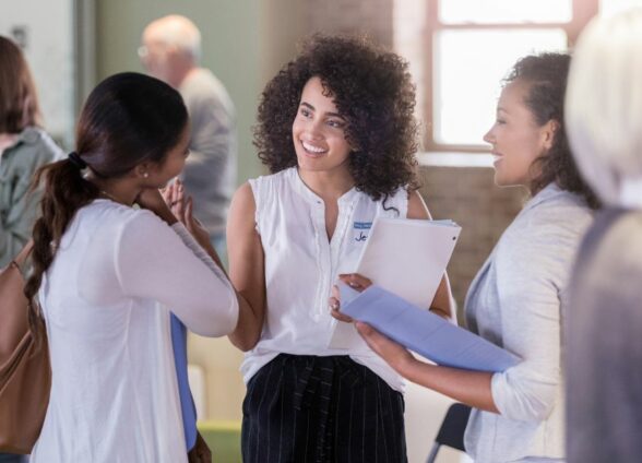 A group of women are having a conversation while standing in a room full of people.
