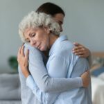 older woman hugs younger person and rests her her head on their shoulder