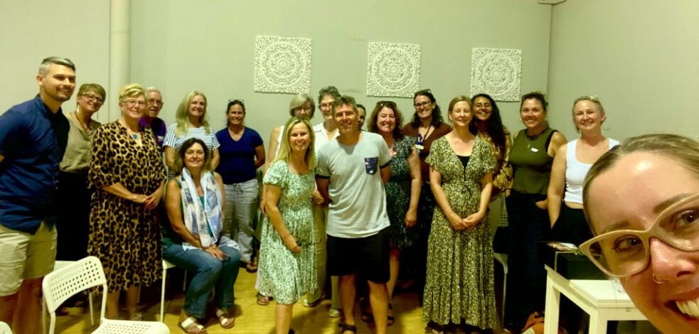 A group of 20 practitioners stand together for a photo after a network meeting presentation.