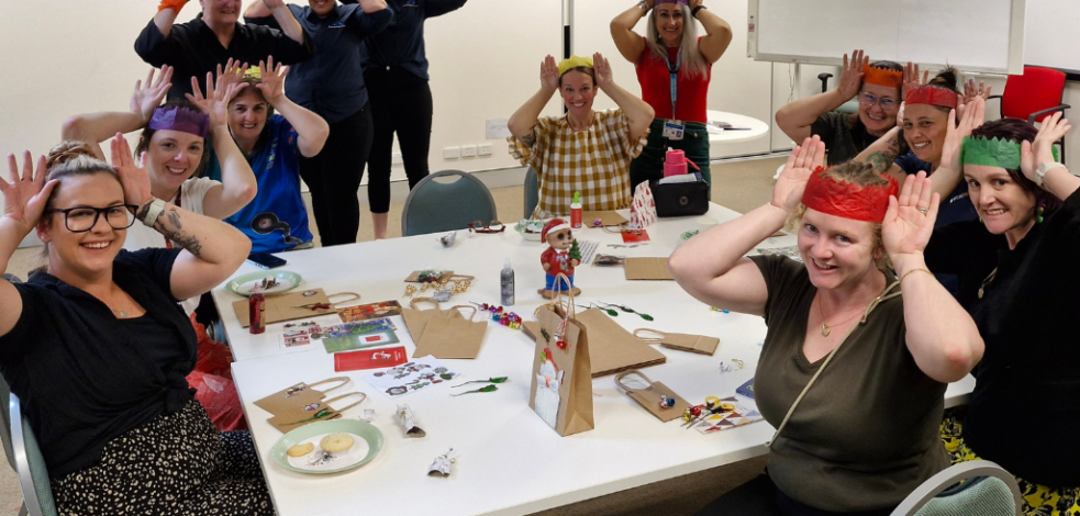 A group of practitioners sit around a table of Christmas themed craft supplies, having fun and making hats.