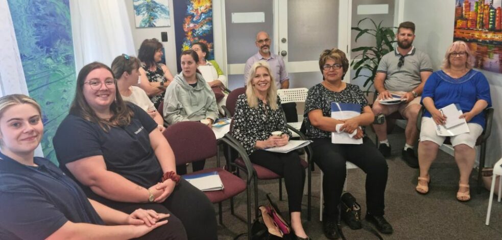A group of ten practitioners sit on chairs in a semi-circle ready to watch a series of presentations.