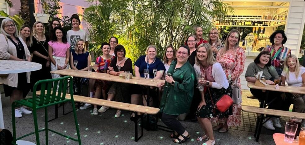 A big group of practitioners gather around some tables in the outdoor area of a restaurant, smiling at the camera for a photo.
