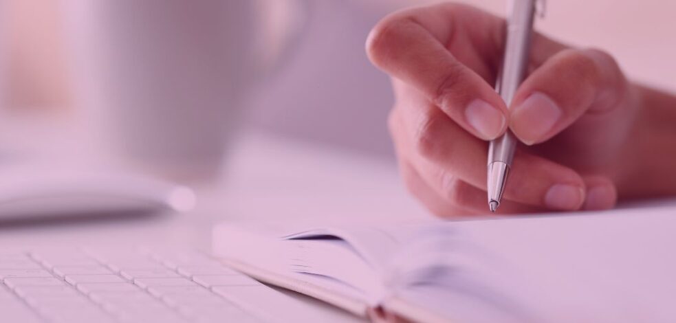 A close up of a hand holding a pen, writing in a notebook.