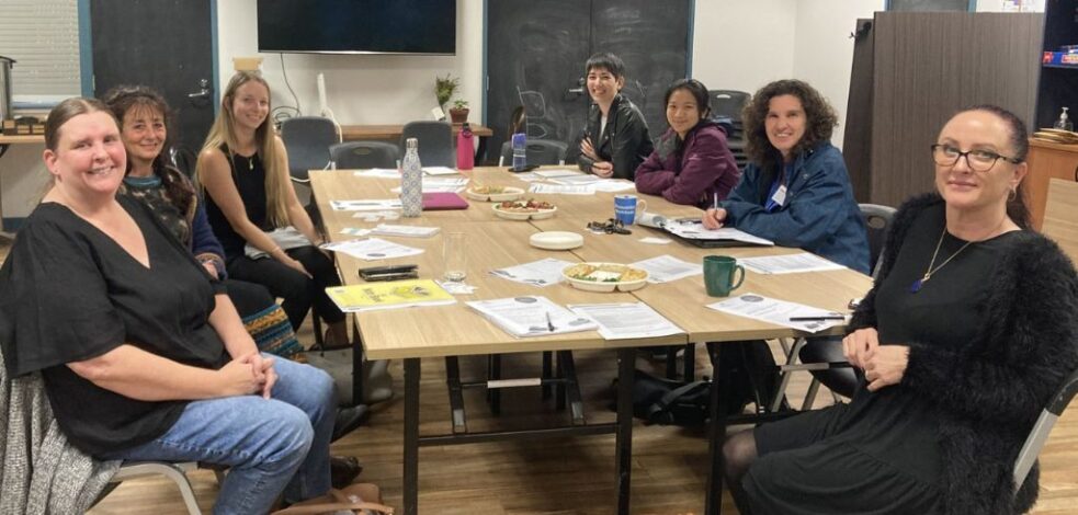 A group of practitioners sit around a meeting room table, smiling for a photo.
