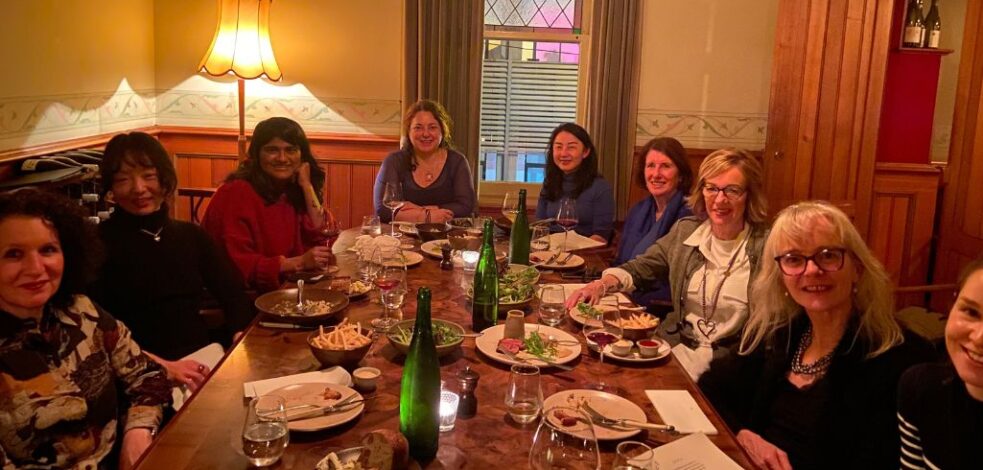A group of practitioners gather around a restaurant table with food for their network meeting.