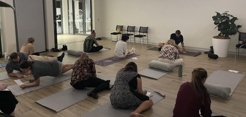 A group of people participating in yoga while making notes.