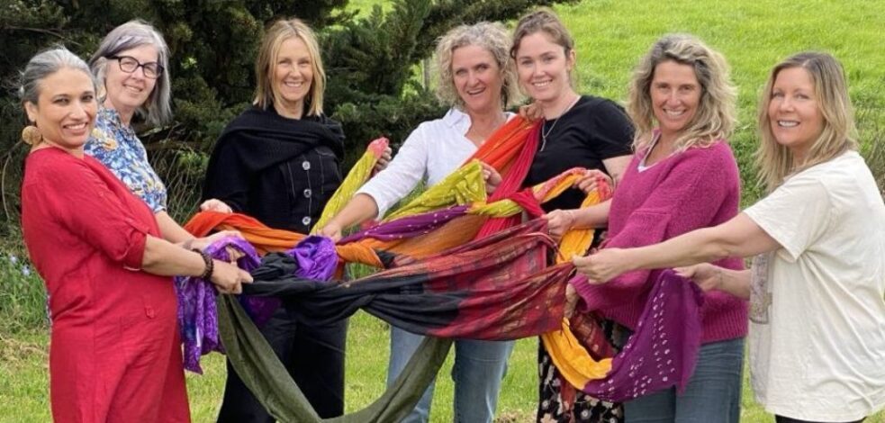 A group of practitioners in colourful clothes, stand together outside undertaking an activity with tangled scarves.